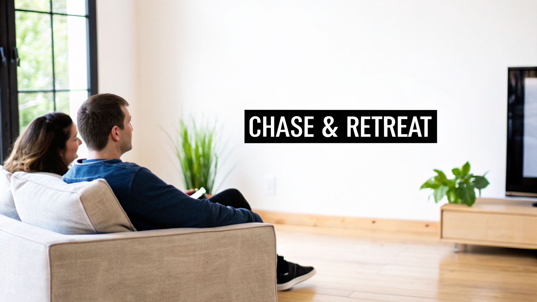 A couple sits on a beige couch, looking at a wall with "CHASE & RETREAT" text.