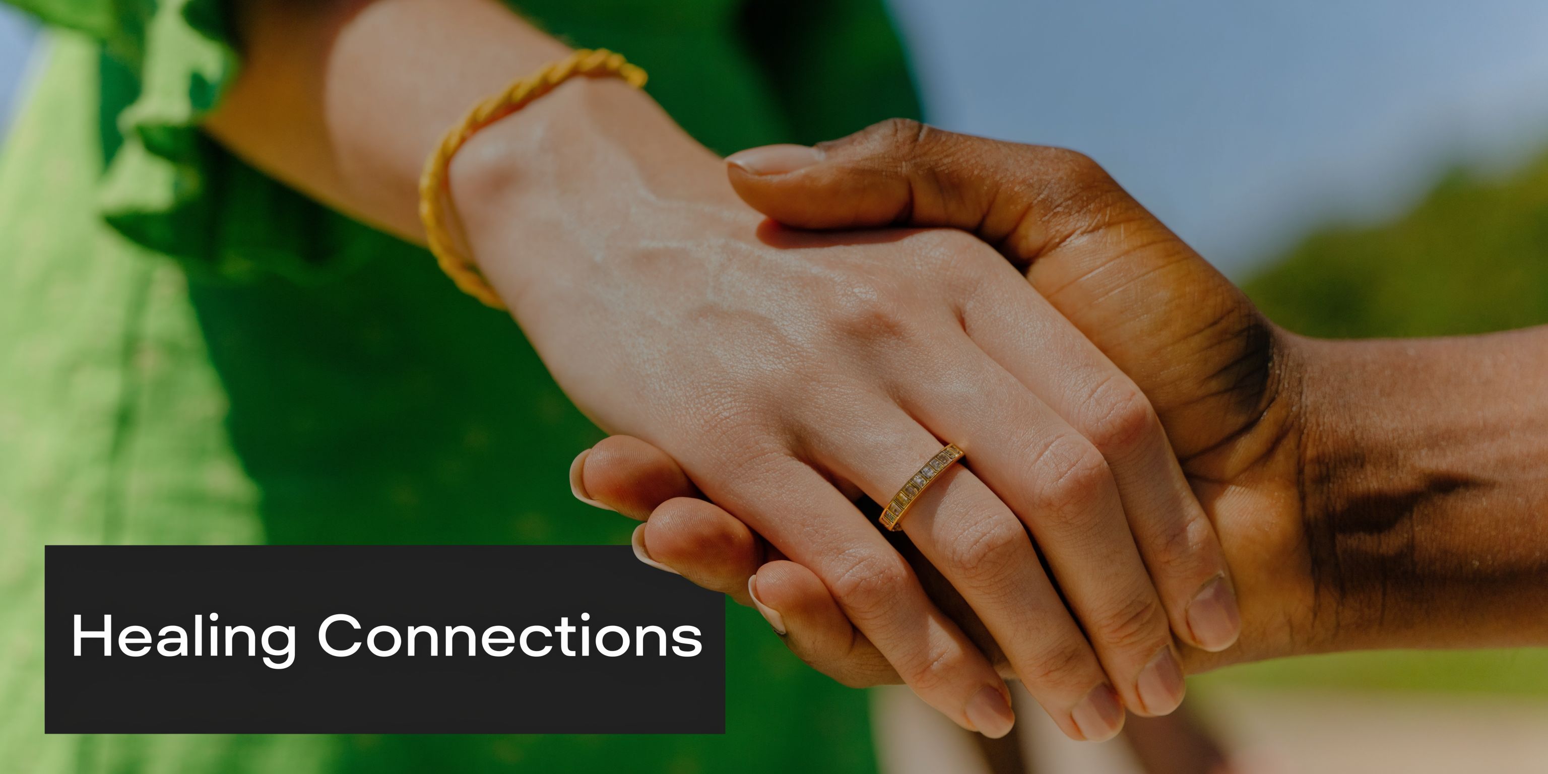 A close-up view of two hands of different skin tones holding each other warmly outdoors.