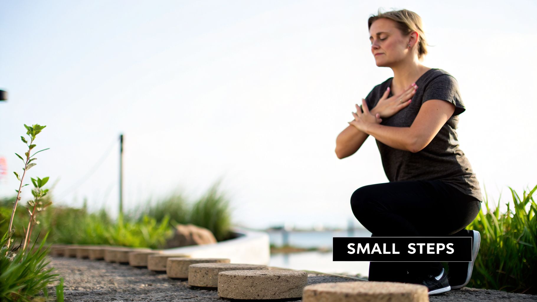 A woman in a dark shirt and pants performs a yoga pose outdoors next to a path of small steps.