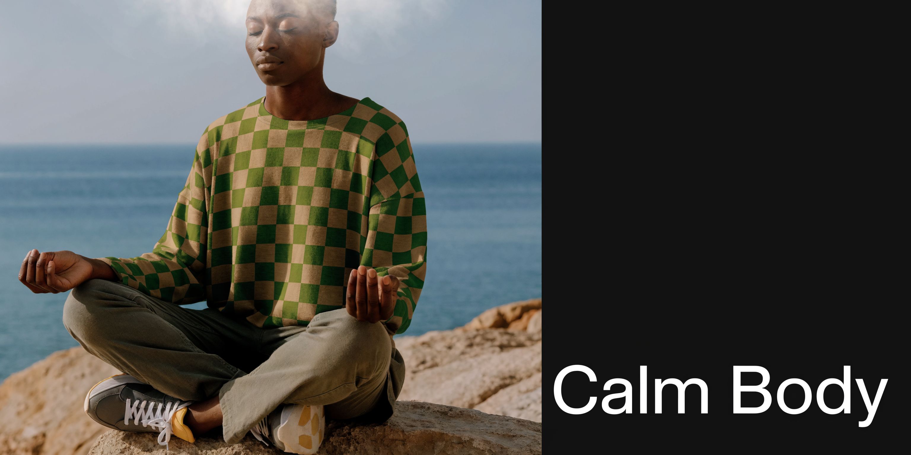A person with a calm expression meditating in a checkerboard shirt while sitting on a cliffside.