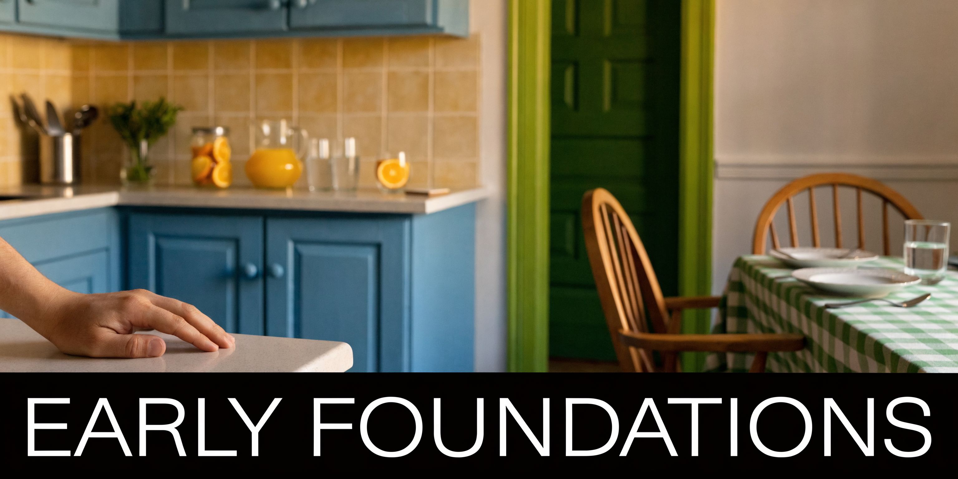 A hand rests on a clean kitchen counter near a dining table set for a quiet meal.