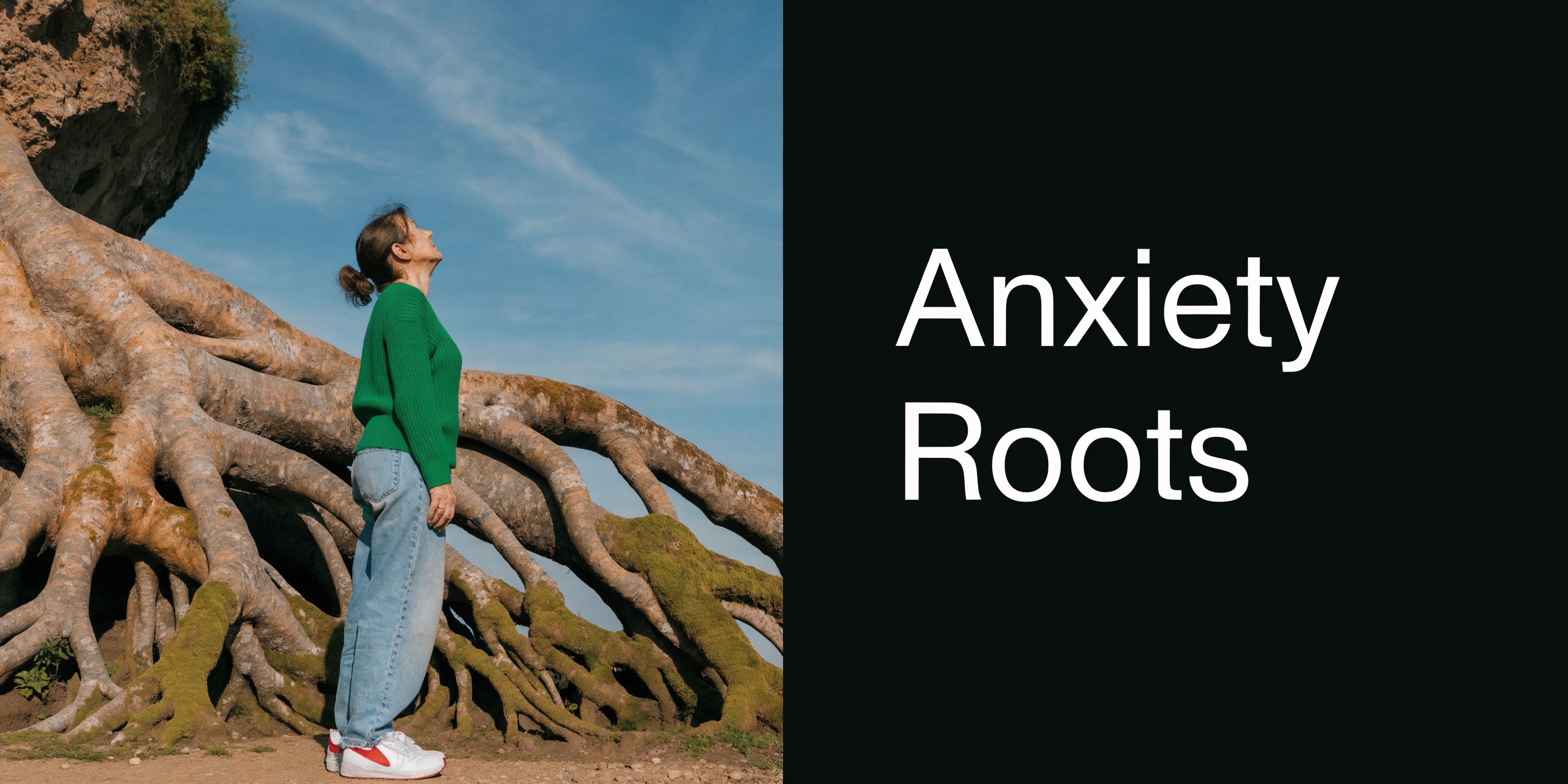 A woman in a green sweater looks up towards the sky while standing near ancient tree roots.