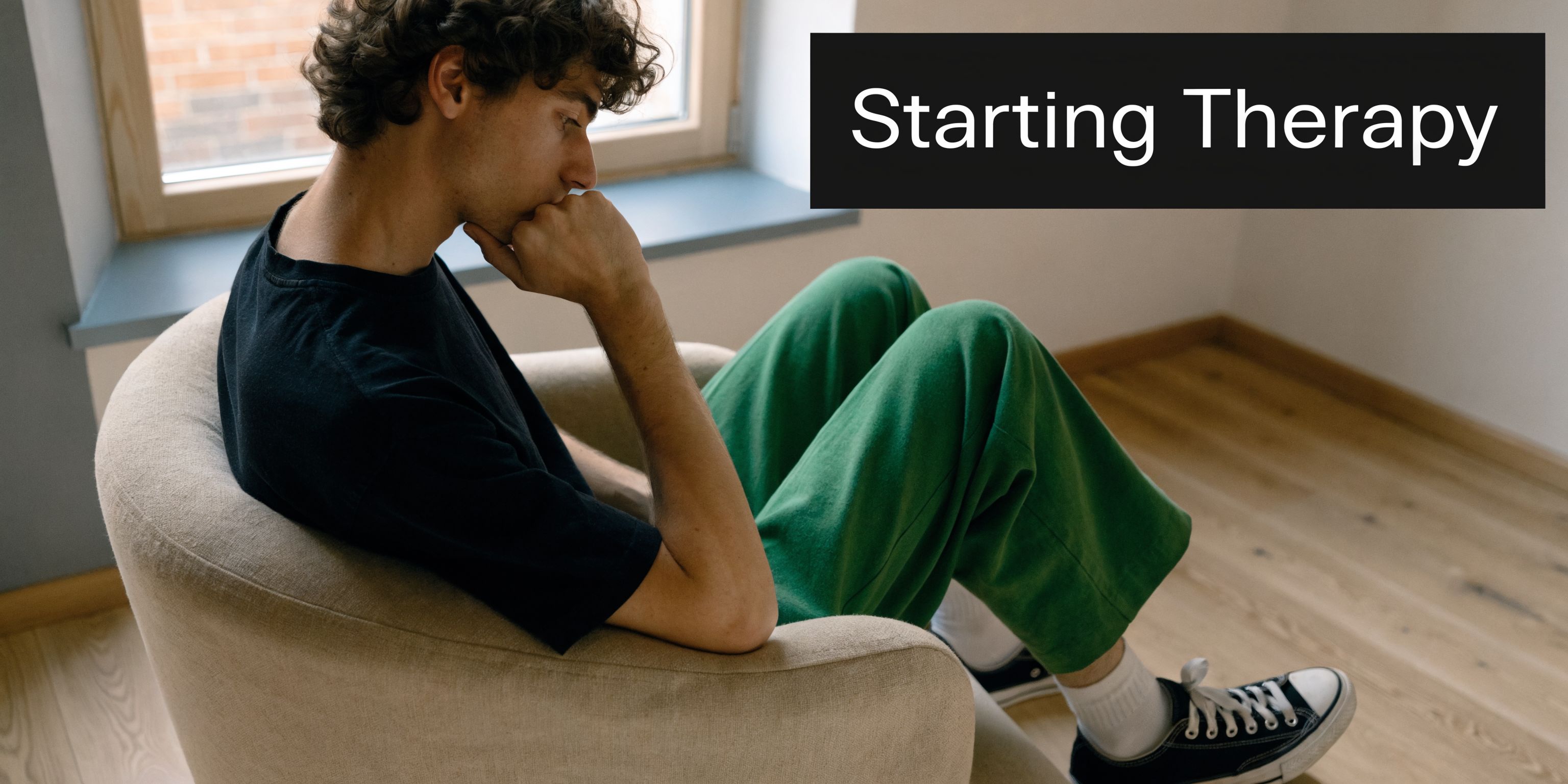 A young man with curly hair sits in a chair, looking thoughtful while starting therapy sessions.