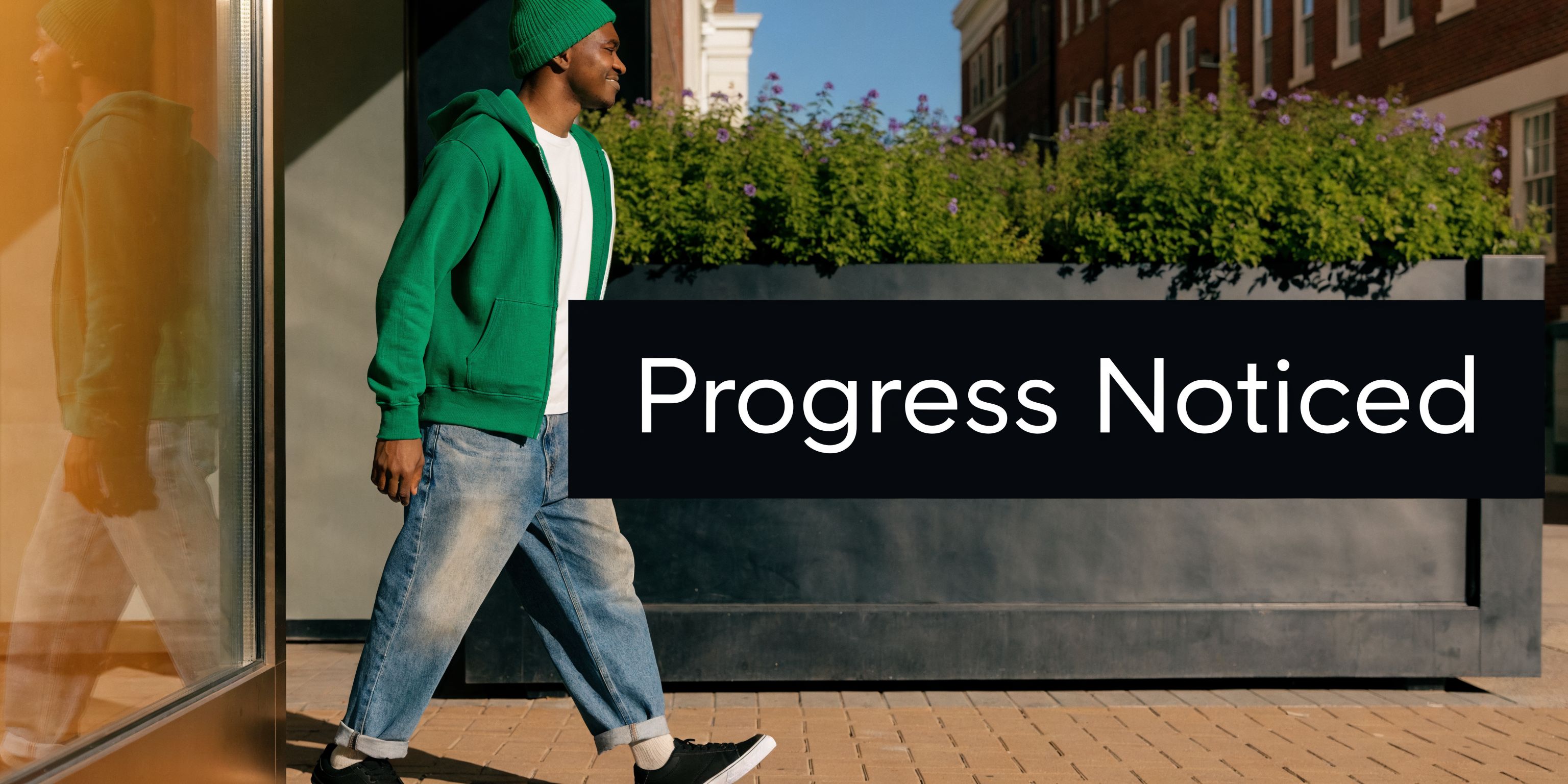 A happy young man in a green hoodie and beanie walking outside during a sunny day.