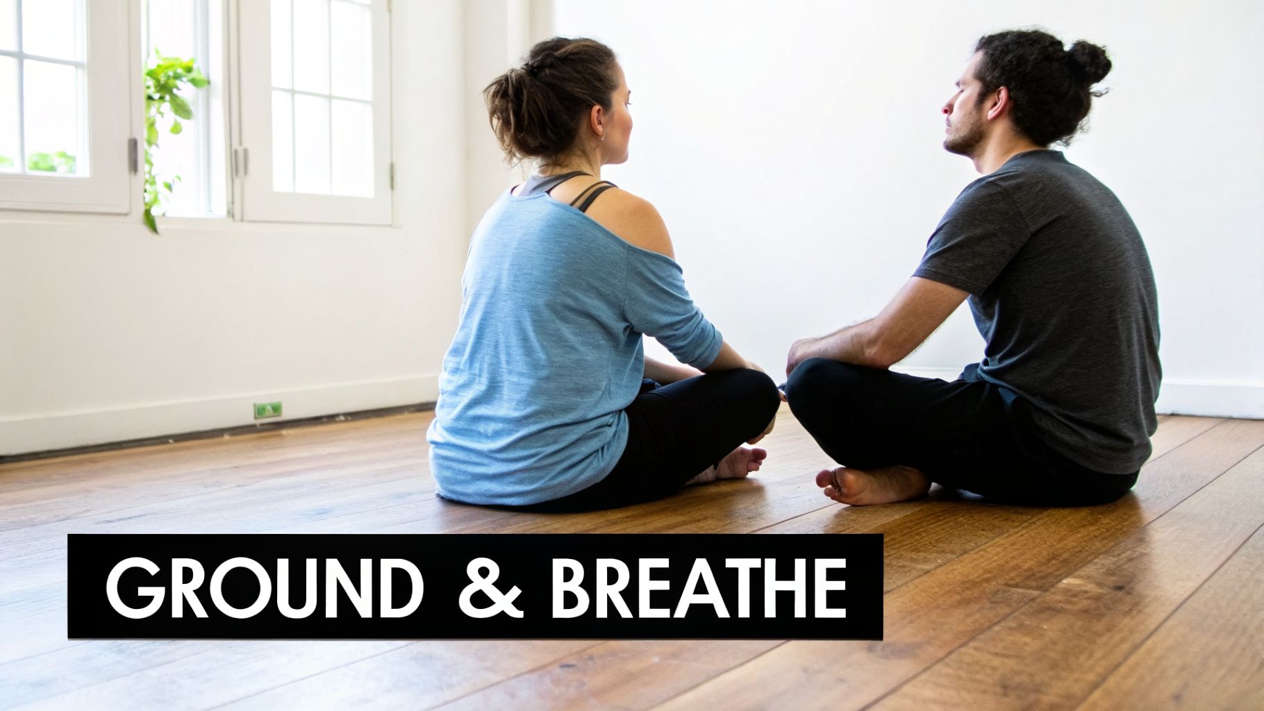 Two people sit on a wooden floor facing each other, meditating peacefully.